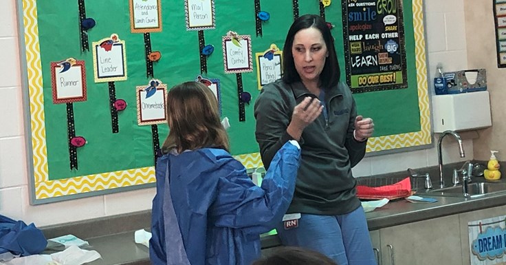 Michelle Tingley showing a student how to put on a surgical gown