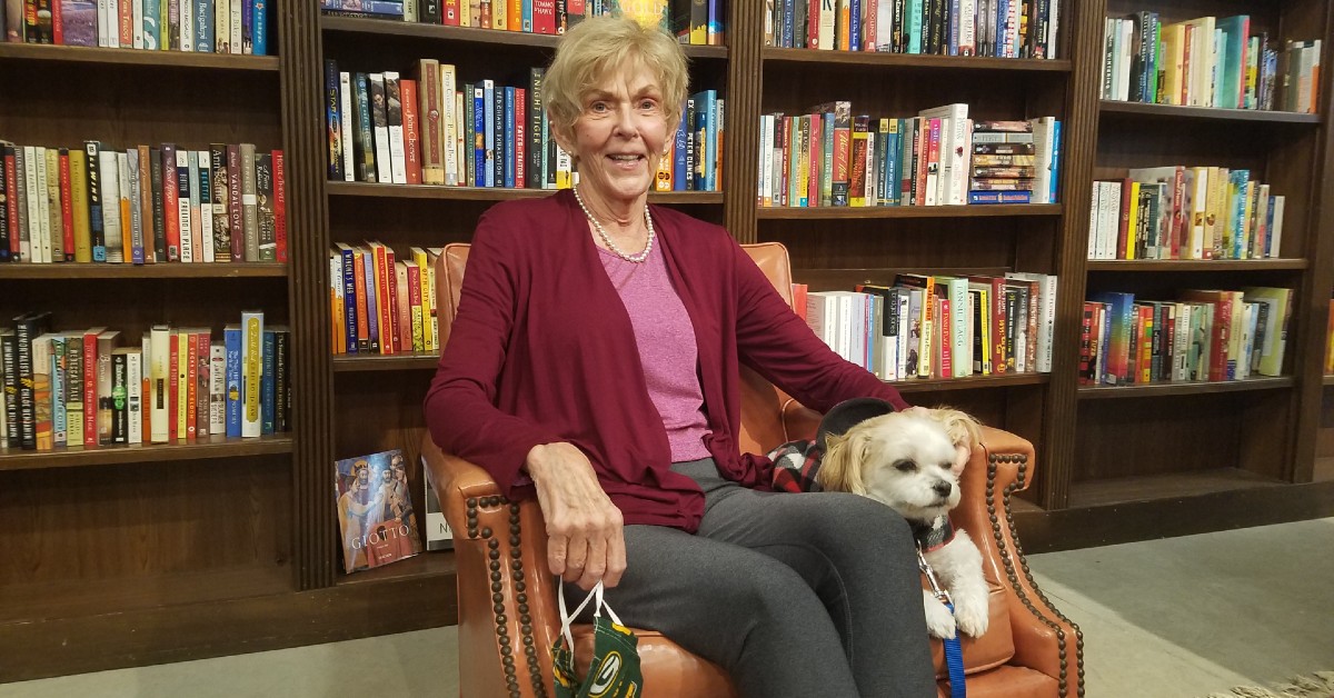 Joan Barry sits in a chair in front of a large bookcase.