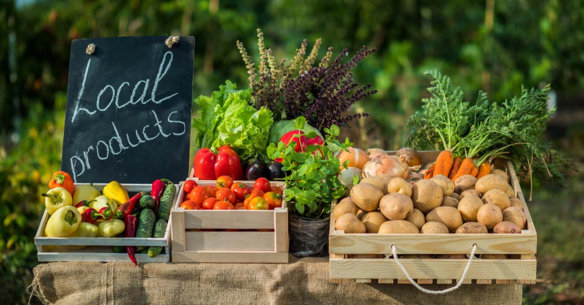 Peppers, tomatoes, greens, carrots and potatoes in crates at a farmers market.