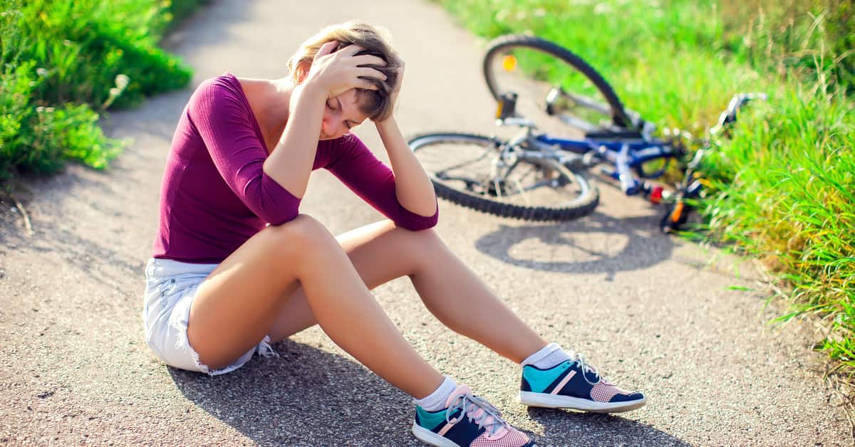 Cyclist sitting on pavement holding head in both hands