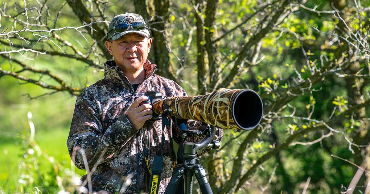 Photo of Dr. Xinqian Chen behind a long-lens camera. He is dressed in outdoors attire.